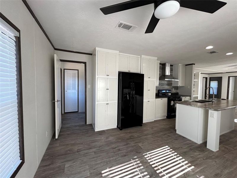 Kitchen featuring black appliances, white cabinets, wall chimney exhaust hood, dark countertops, and crown molding