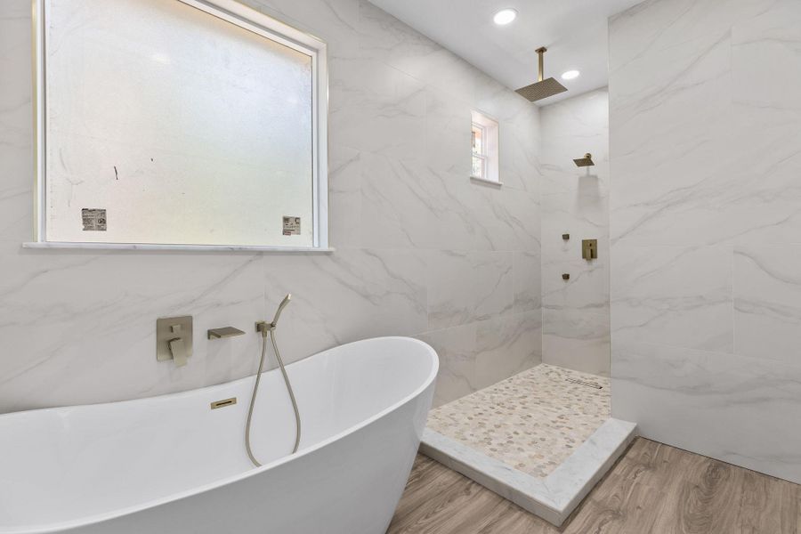 Bathroom with a freestanding tub, a marble finish shower, recessed lighting, light wood-style floors, and tile walls