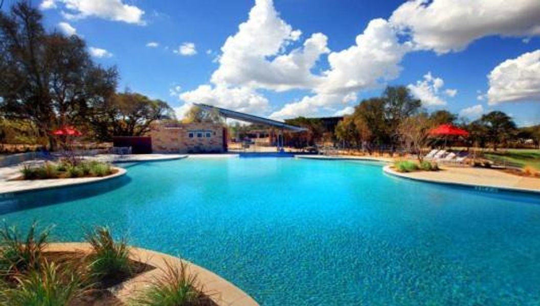 Expansive resort-style swimming pool featuring a curved concrete deck, integrated tanning ledges, and surrounding mature landscaping Expansive resort-style swimming pool featuring a curved concrete deck, integrated tanning ledges, and surrounding mature landscaping