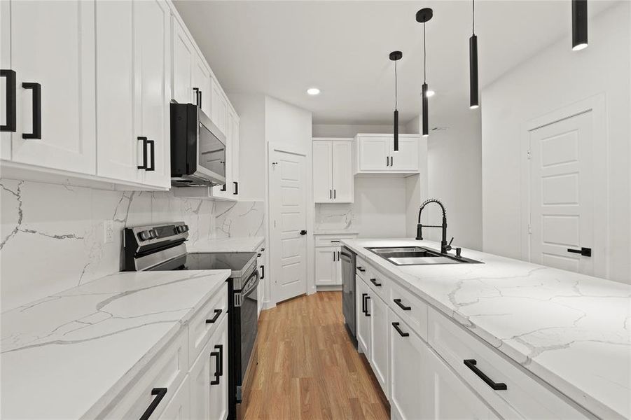 Kitchen featuring sink, pendant lighting, stainless steel appliances, light stone countertops, and white cabinets