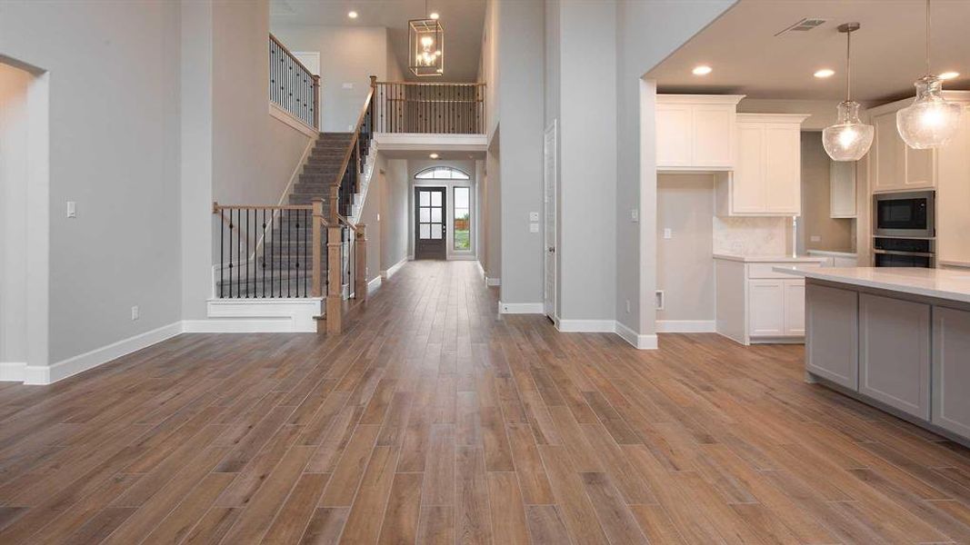 Great room featuring white cabinetry, decorative light fixtures, black microwave, oven, and light hardwood / wood-style floors