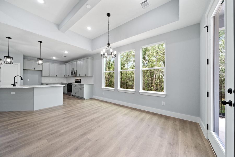 Open-concept living space featuring wood-finish flooring, a contemporary kitchen with light cabinetry, ample natural light from multiple windows, and a glass-paneled door