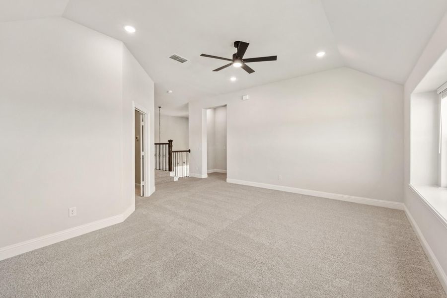 Empty bonus room with vaulted ceiling, ceiling fan, carpet flooring, and staircase railing visible in background. Empty bonus room with vaulted ceiling, ceiling fan, carpet flooring, and staircase railing visible in background.