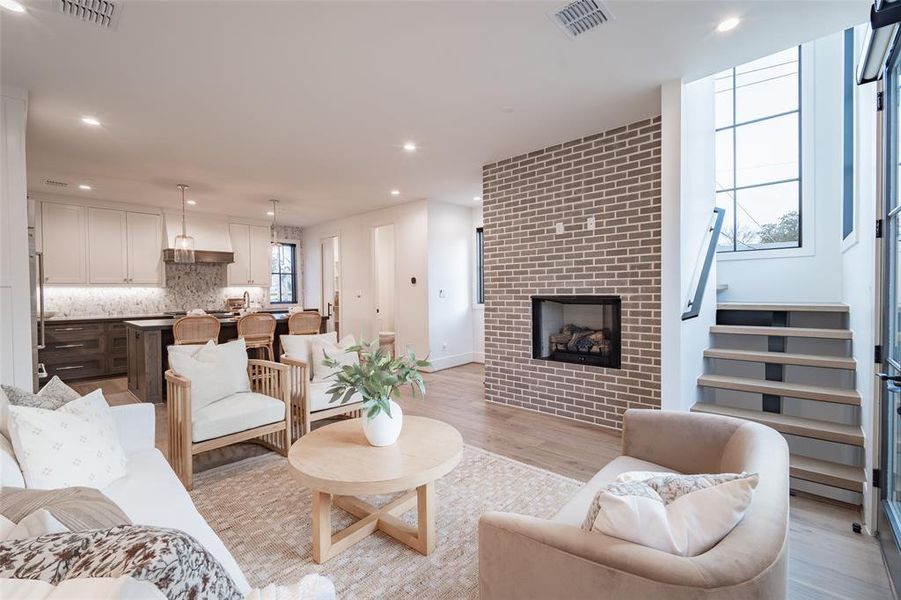 Living room with brick wall, a fireplace, and light hardwood / wood-style flooring