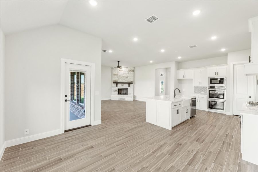 Open-concept kitchen and living area with white cabinets, kitchen island, stone fireplace, and wood-look tile floors Open-concept kitchen and living area with white cabinets, kitchen island, stone fireplace, and wood-look tile floors