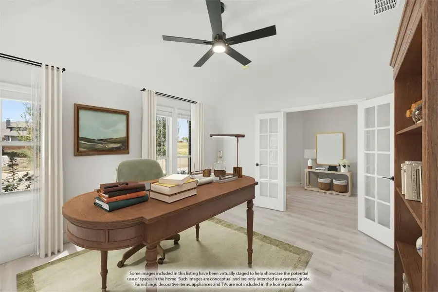 Home office with vaulted ceiling, wood desk, ceiling fan, and French doors leading to an adjacent room