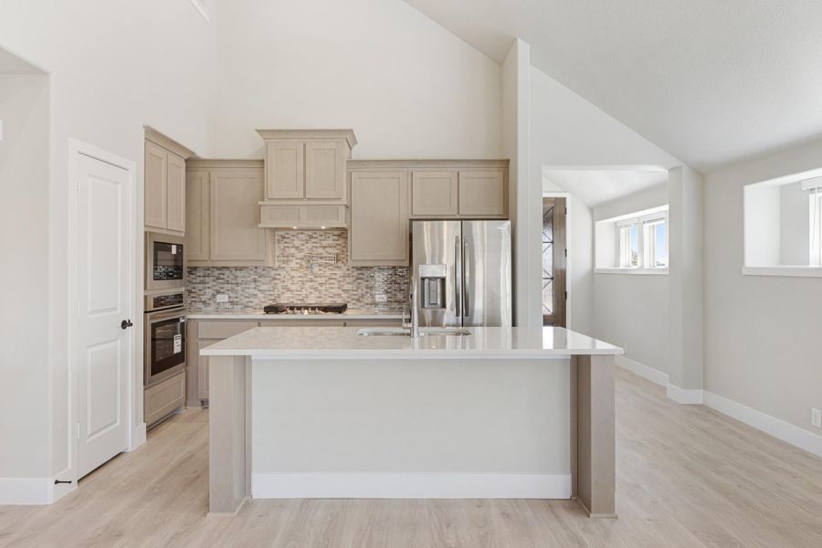 Kitchen with center island, beige cabinets, tile backsplash, stainless steel appliances, and vaulted ceiling