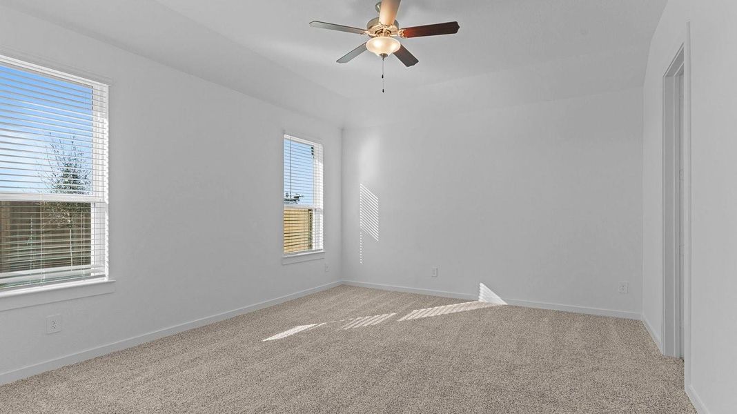 Primary bedroom with ceiling fan, plush carpeting, and a large walk-in closet.