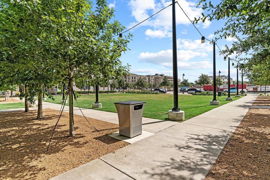 Expansive green space featuring a concrete pathway, mature trees, string lighting, and a manicured lawn
