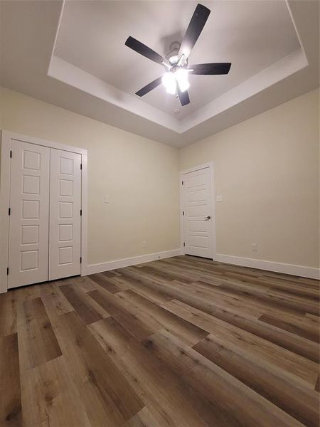 Spare room featuring a box tray ceiling, dark wood luxury vinyl flooring, and 9' high with designer ceiling fan.