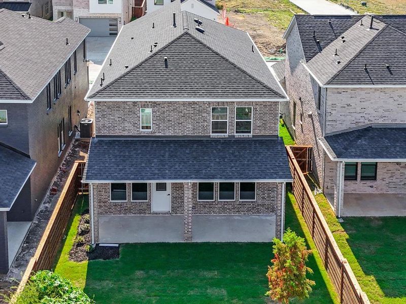 Rear view of house featuring roof with shingles, brick siding, and a fenced backyard