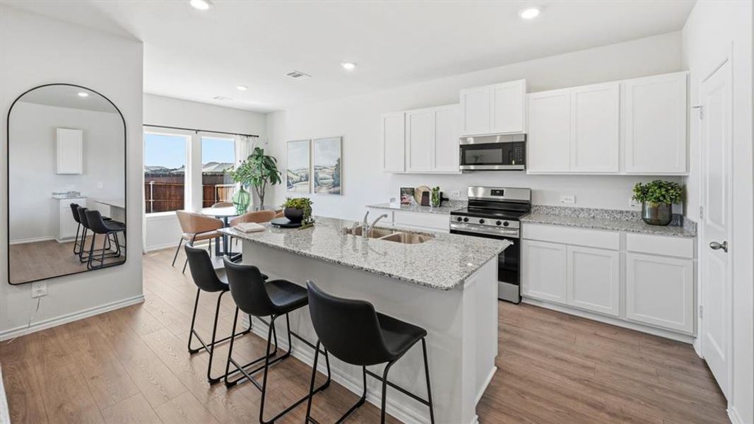 Kitchen with stainless steel appliances, light stone counters, white cabinets, light wood-style floors, and a kitchen breakfast bar Kitchen with stainless steel appliances, light stone counters, white cabinets, light wood-style floors, and a kitchen breakfast bar
