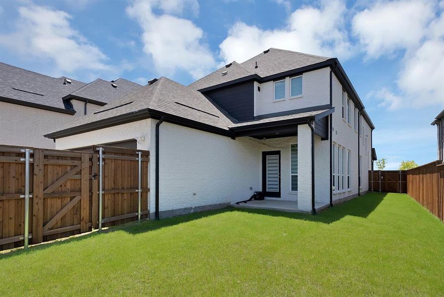 Spacious backyard featuring a manicured lawn, full privacy fencing, and a covered patio area