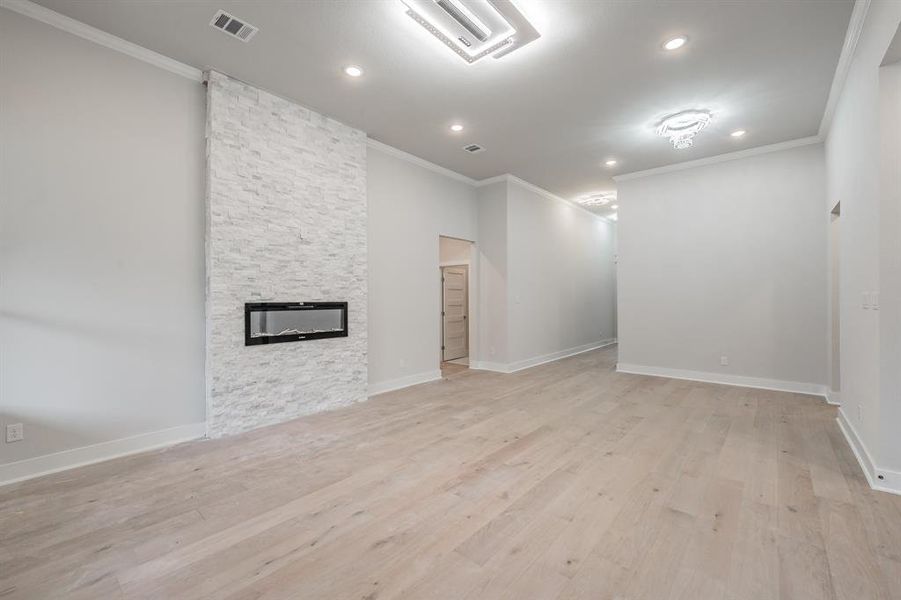 Unfurnished living room with ornamental molding, a stone fireplace, light wood-style flooring, and recessed lighting