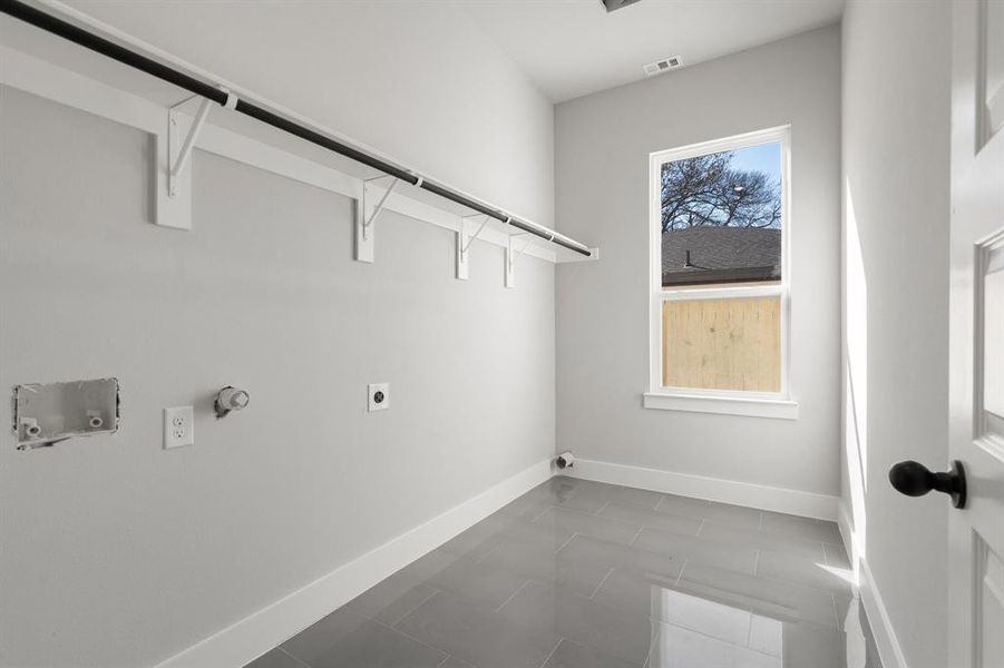 Clothes washing area featuring hookup for a gas dryer, plenty of natural light, hookup for an electric dryer, and dark tile patterned flooring