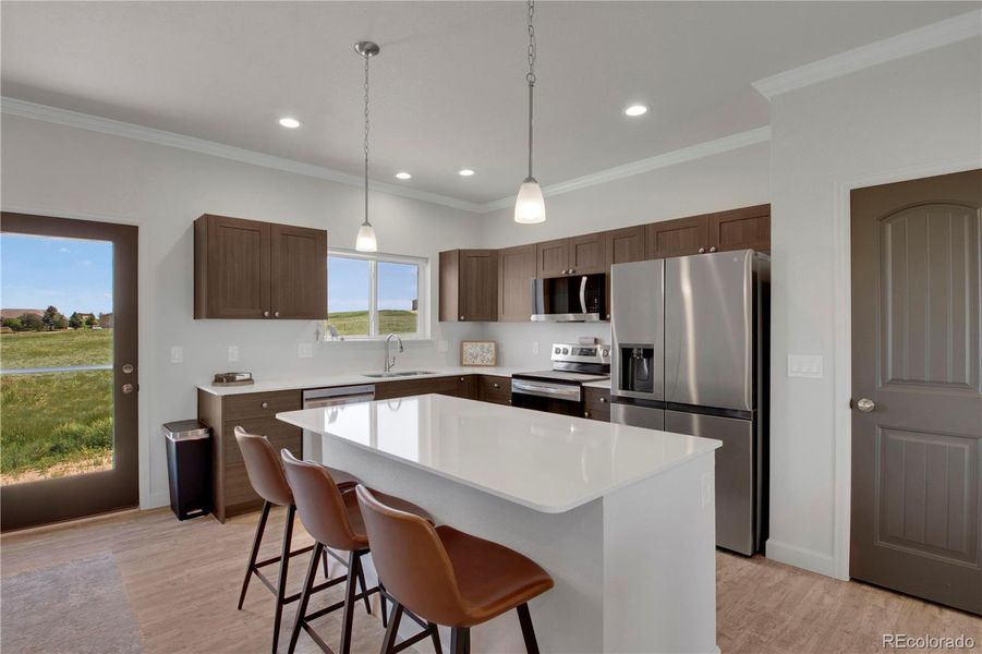 Kitchen featuring appliances with stainless steel finishes, light wood-style flooring, crown molding, a kitchen breakfast bar, and a center island