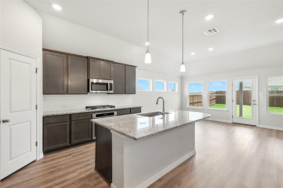 Kitchen with dark brown cabinetry, light wood finished floors, light stone countertops, appliances with stainless steel finishes, and decorative backsplash