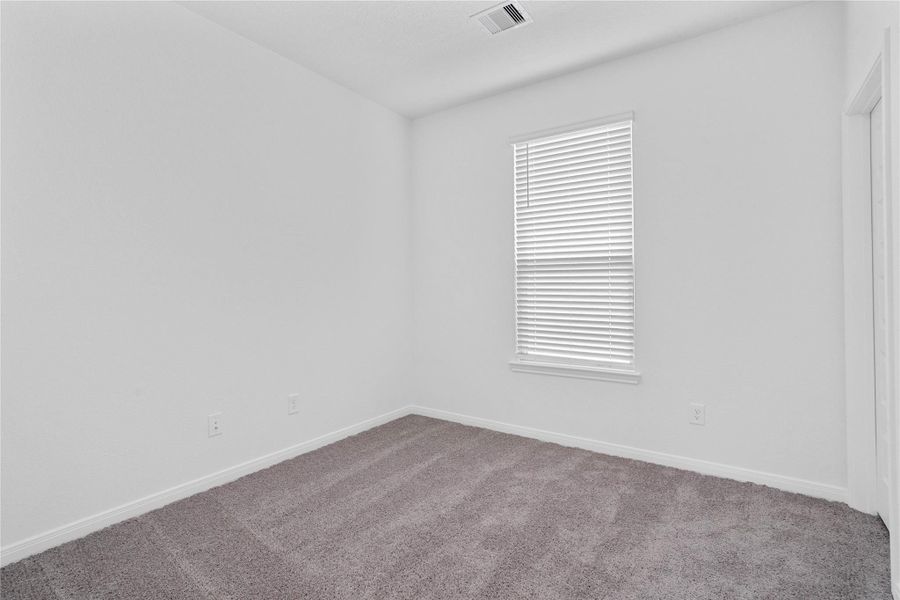 One of the three secondary bedrooms, pictured here, offers comfort and style with plush carpeting, neutral paint tones, recessed lighting, a large window with fitted blinds, and a walk-in closet.