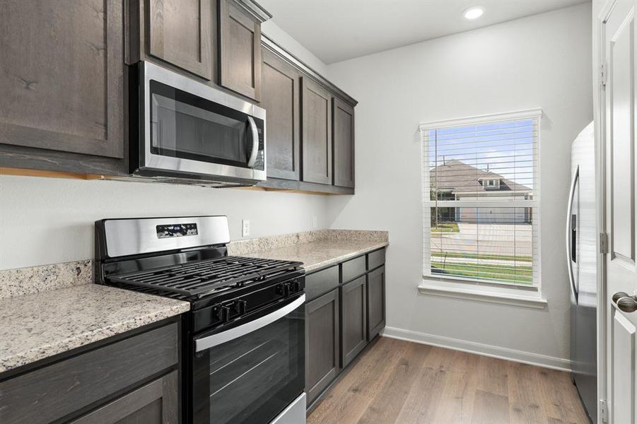 Kitchen with stainless steel appliances, light stone countertops, light wood-type flooring, dark brown cabinets, and recessed lighting