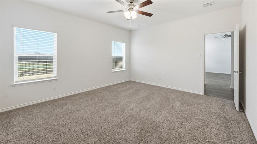 Spacious room featuring neutral carpet flooring, two windows with blinds, a ceiling fan with light fixture, and white painted walls