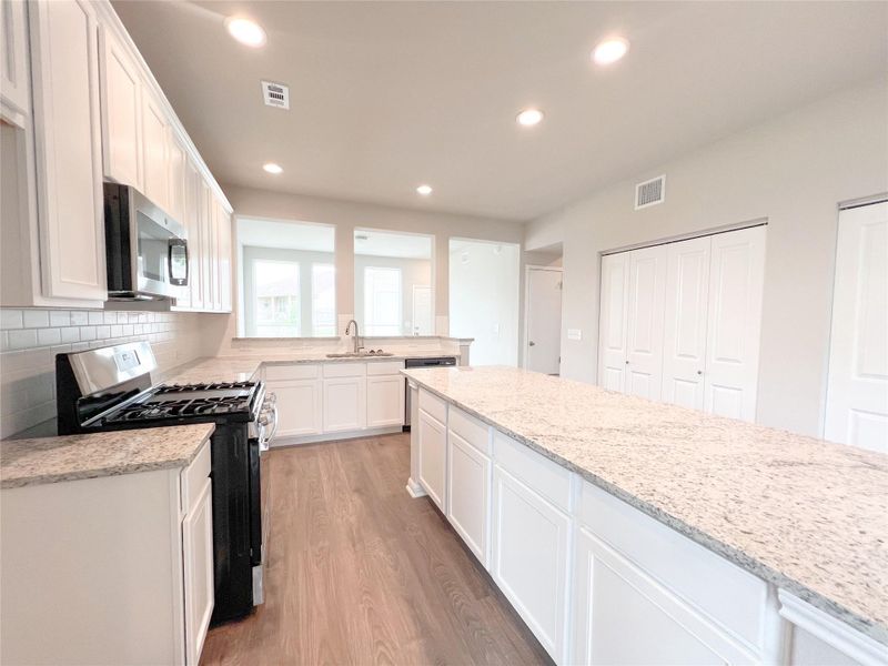Kitchen featuring gas stove, white cabinetry, stainless steel microwave, light wood-type flooring, and tasteful backsplash