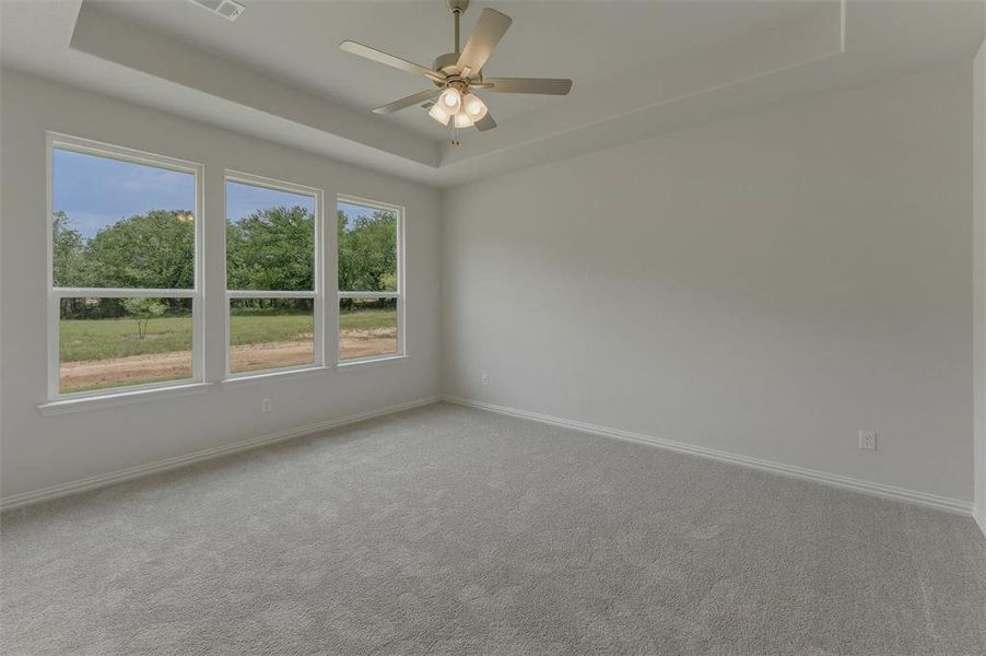 Spacious room featuring three large windows, a tray ceiling, and a ceiling fan with integrated lighting