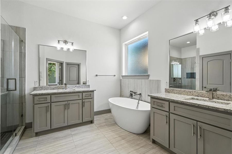 Bathroom featuring a stall shower, healthy amount of natural light, two vanities, and a freestanding tub Bathroom featuring a stall shower, healthy amount of natural light, two vanities, and a freestanding tub