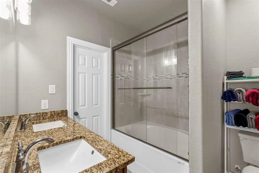 Primary bathroom with bath / shower combo with glass door, double vanity, and toilet