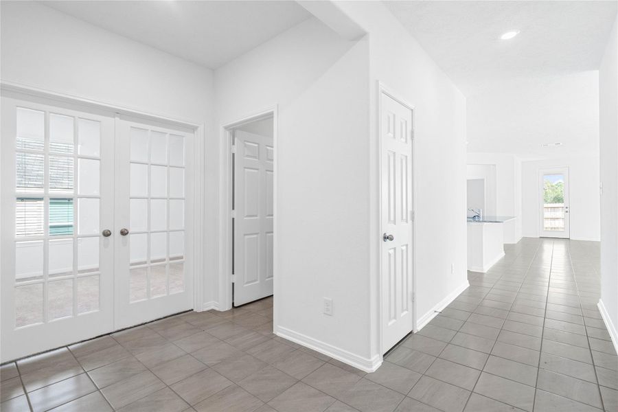 Flowing entry hallway featuring durable tile flooring, providing access to essential areas like the laundry room before opening up to the private Den via stylish double French doors.