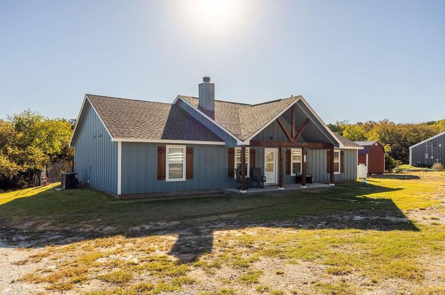 Back of house featuring a patio, a chimney, roof with shingles, and a lawn