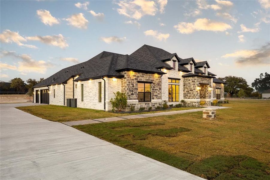 View of front of house with stone siding, a front lawn, roof with shingles, concrete driveway, and a garage View of front of house with stone siding, a front lawn, roof with shingles, concrete driveway, and a garage