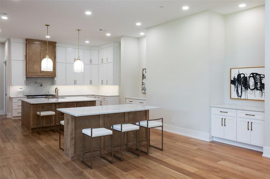 Kitchen featuring decorative light fixtures, an island with sink, white cabinets, a kitchen breakfast bar, and hardwood / wood-style flooring