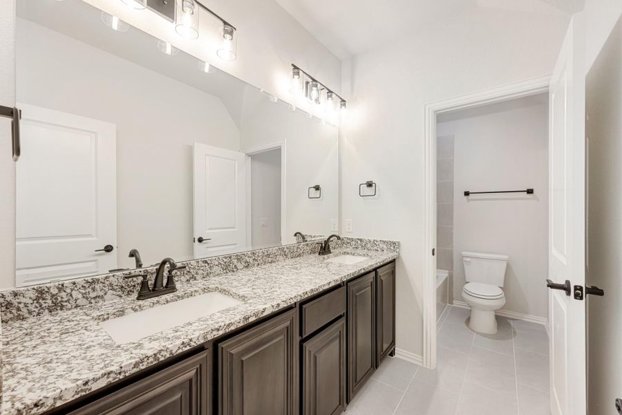 Bathroom with double sink vanity, granite countertops, dark cabinets, and separate toilet room