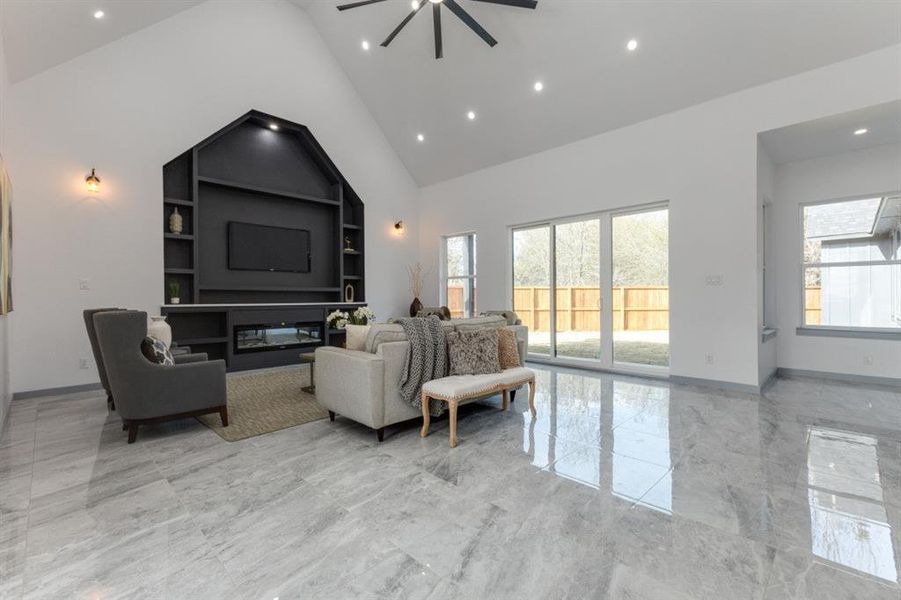 Living room with ceiling fan, high vaulted ceiling, and built in shelves