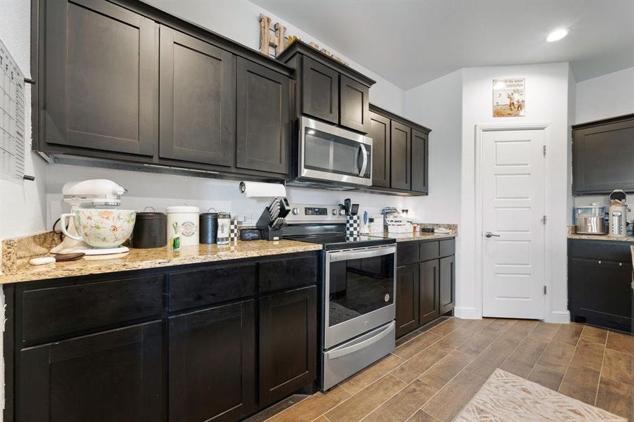 Kitchen featuring stainless steel appliances, wood finish floors, and light stone countertops Kitchen featuring stainless steel appliances, wood finish floors, and light stone countertops