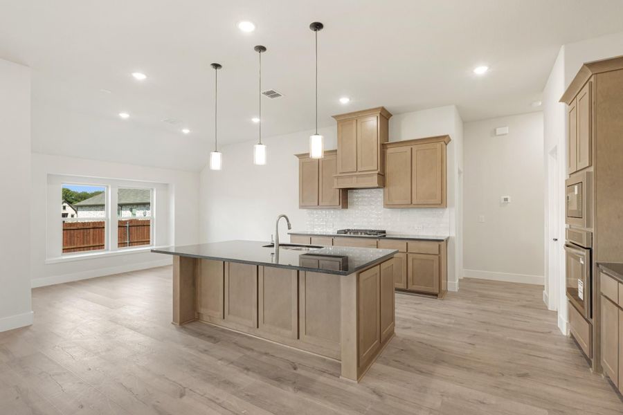 Kitchen with large center island, dark countertops, light wood cabinets, and pendant lights over hardwood floors