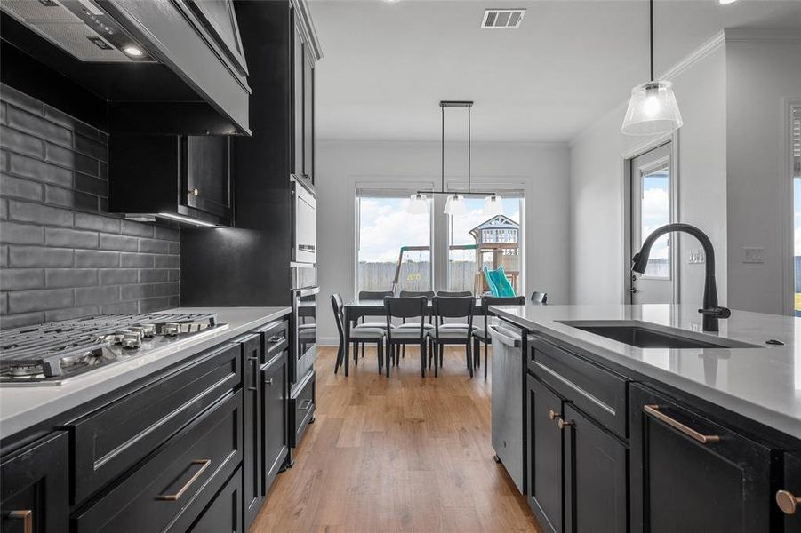 Kitchen with dark cabinets, hanging light fixtures, light stone counters, light wood-style flooring, and ornamental molding Kitchen with dark cabinets, hanging light fixtures, light stone counters, light wood-style flooring, and ornamental molding