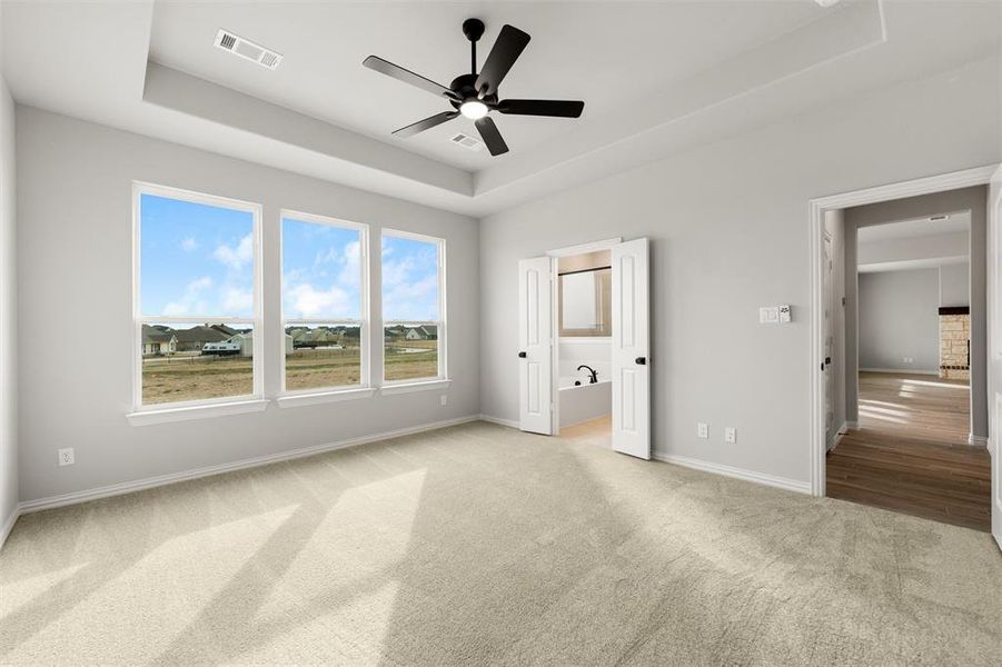 Unfurnished bedroom featuring a raised ceiling, a ceiling fan, light colored carpet, and ensuite bath Unfurnished bedroom featuring a raised ceiling, a ceiling fan, light colored carpet, and ensuite bath