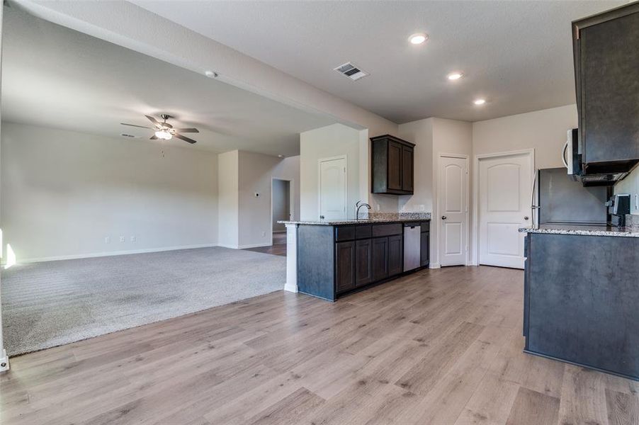 Kitchen featuring light stone countertops, open floor plan, ceiling fan, dark wood finish cabinets, and light wood-type flooring