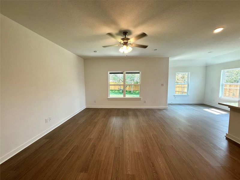 Unfurnished living room with healthy amount of natural light, dark wood-style flooring, a textured ceiling, and ceiling fan Unfurnished living room with healthy amount of natural light, dark wood-style flooring, a textured ceiling, and ceiling fan