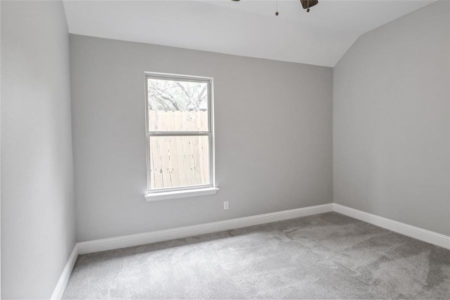 Carpeted spare room with ceiling fan and vaulted ceiling