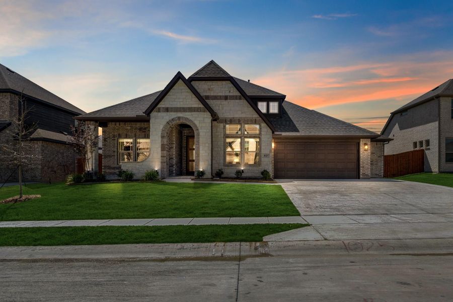 Single-story home with brick and stone exterior, arched entry, two-car garage, and green lawn at dusk.