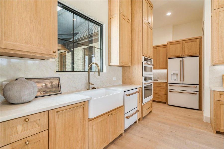 An inviting culinary space offers light wood cabinetry, pristine countertops, and modern integrated appliances.