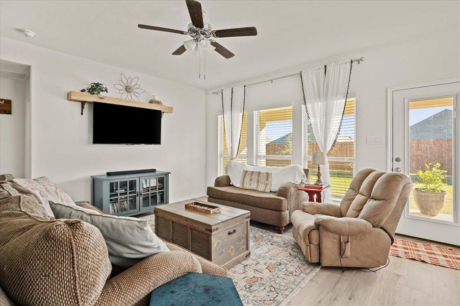 Living room featuring light wood-type flooring, ceiling fan, and a healthy amount of sunlight