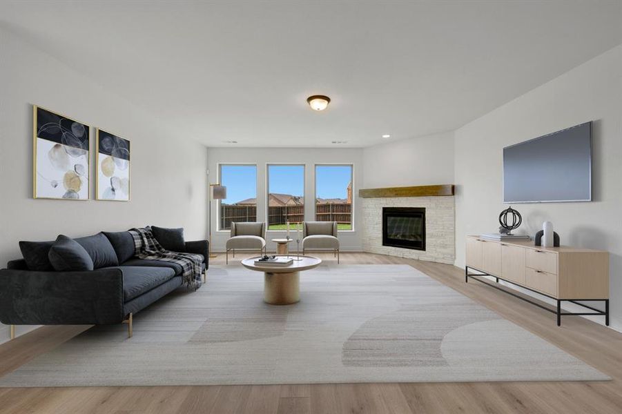 Spacious room featuring wood-finish flooring, a corner fireplace with a stone surround and wood mantle, and three large windows