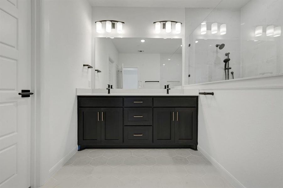 Dual vanity with black cabinetry, white countertops, hexagon tile flooring, and a glass-enclosed shower with black fixtures Dual vanity with black cabinetry, white countertops, hexagon tile flooring, and a glass-enclosed shower with black fixtures