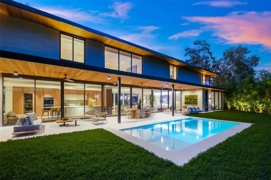 Modern two-story exterior featuring expansive floor-to-ceiling glass wall systems, a recessed wood-paneled ceiling, a rectangular in-ground swimming pool, and stone pool decking