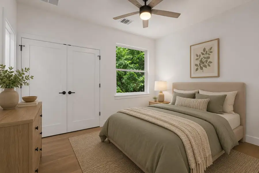 A tranquil primary bedroom features warm wood flooring and abundant natural light from a well-placed window.