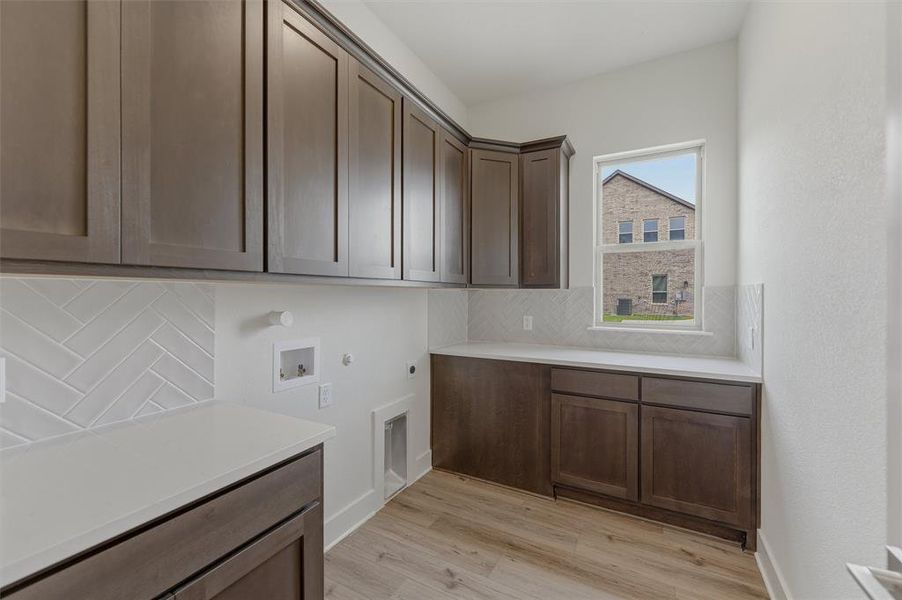 Laundry room featuring extensive upper and lower cabinetry, white countertops, wood-finish flooring, and a white subway tile backsplash in a herringbone pattern