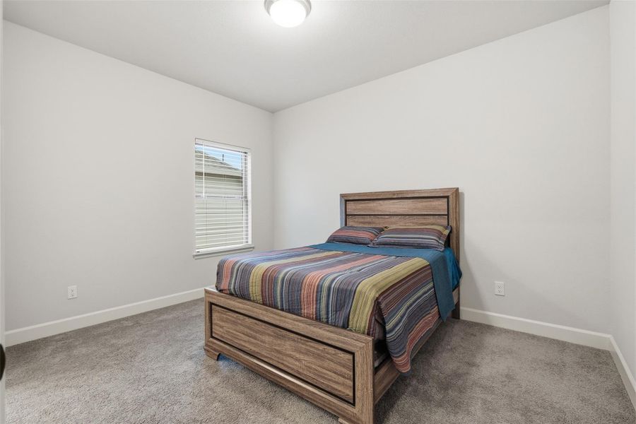 A cozy bedroom with neutral walls and carpet, featuring a window for natural light and a wooden bed with colorful bedding. A cozy bedroom with neutral walls and carpet, featuring a window for natural light and a wooden bed with colorful bedding.